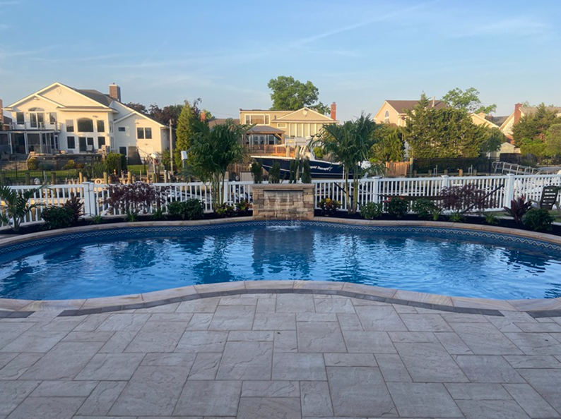 Swimming pool in front of houses, with white picket fence, clear water, and stone patio.