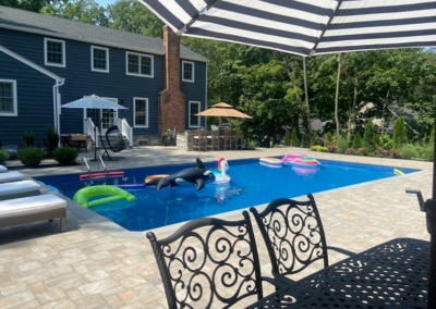 Backyard pool with inflatables, lounge chairs, and a dining area; house in the background.