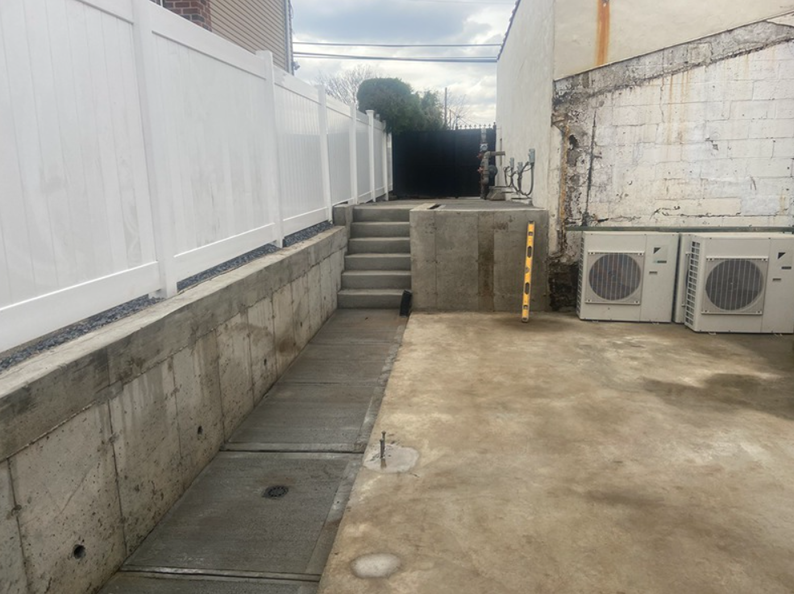 Concrete ramp and stairs alongside a white fence. Two HVAC units are on a building's wall.