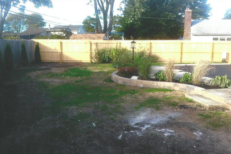 Backyard with a wooden fence, some green grass, and a small garden bed.