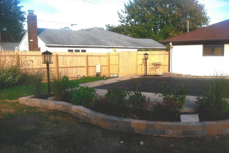 Backyard with a paved area, a brick border garden, wooden fence, and two lamp posts.