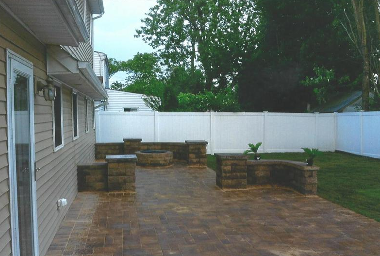 Backyard patio with a fire pit, built-in seating, and a white fence.