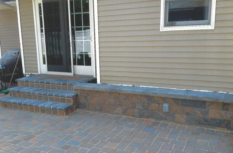 Brick patio with steps leading to sliding glass door; brown and black retaining wall.