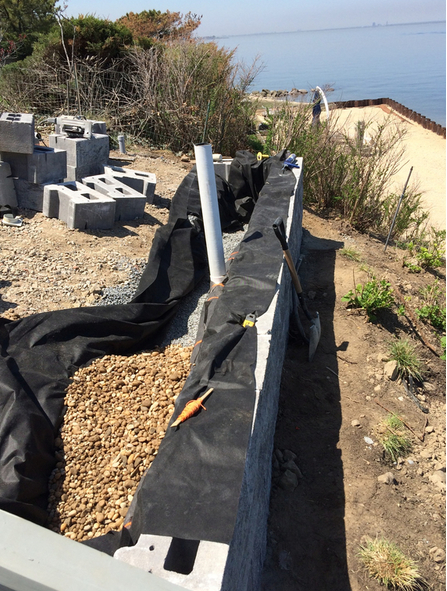 Construction site: a stone wall being built with gravel and black fabric near the ocean.