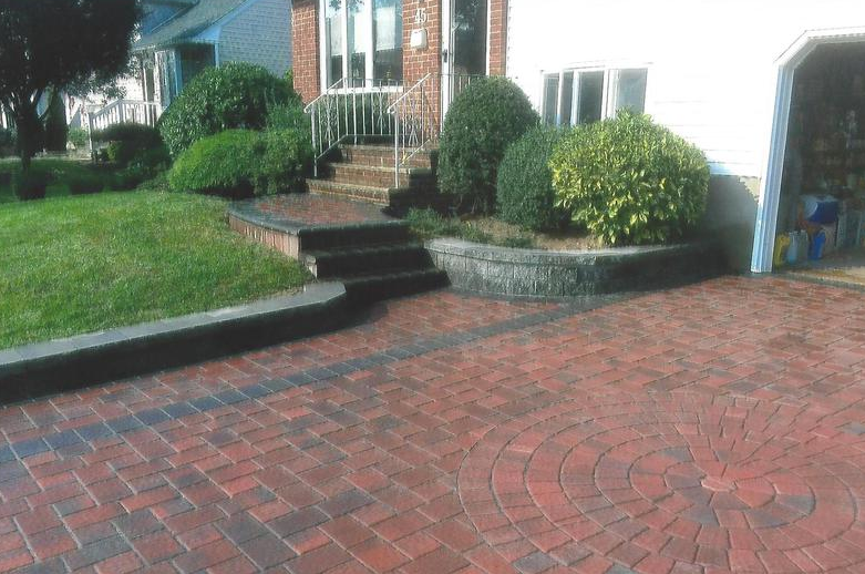 Brick driveway with a circular design, leading to steps and a house with landscaping.