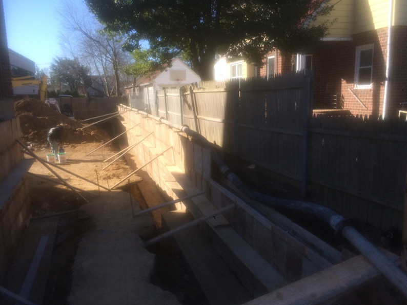 Construction site, trench with wooden supports next to a wooden fence; sunny day.