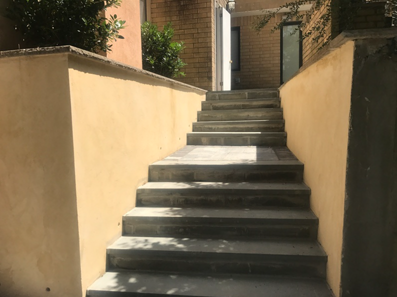 Concrete stairs ascend between yellow walls, leading to a building entrance.