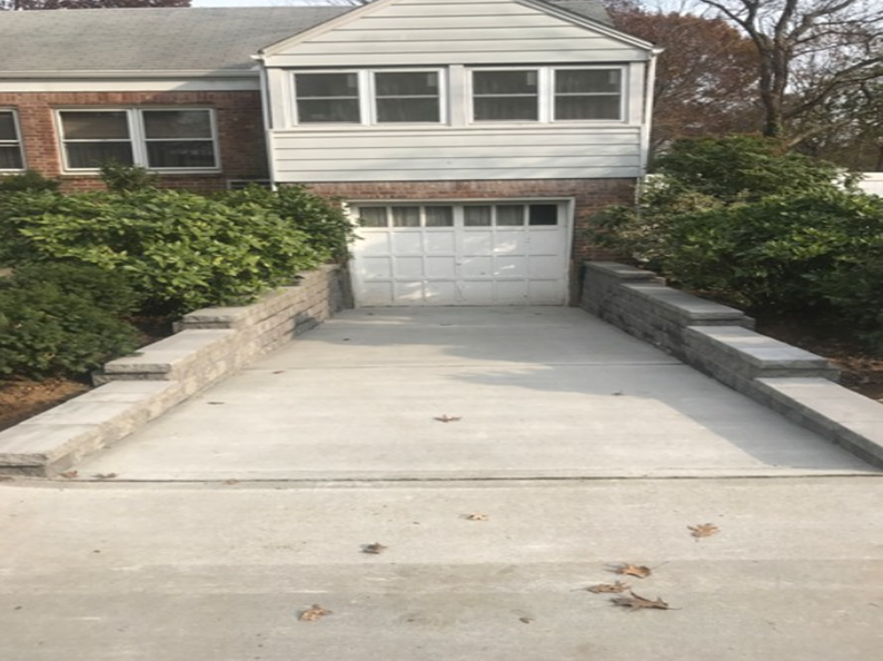 Driveway leading to a garage, flanked by low retaining walls with greenery. The house is brick and white siding.