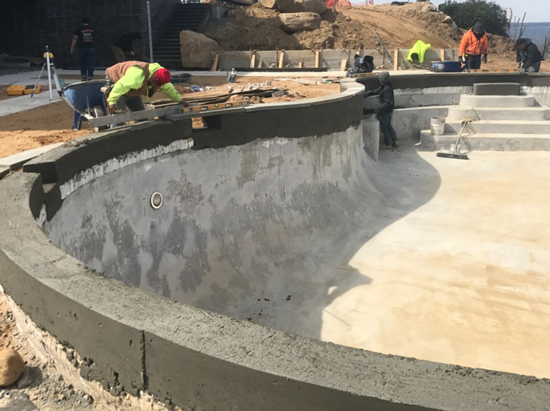Construction workers applying cement to the curved edge of a concrete pool.