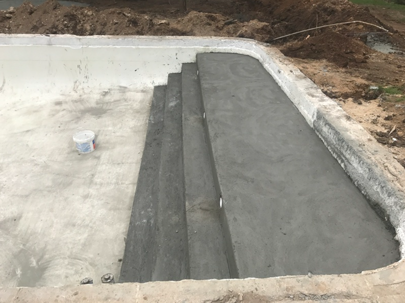 Concrete steps leading into a gray, empty swimming pool under construction.