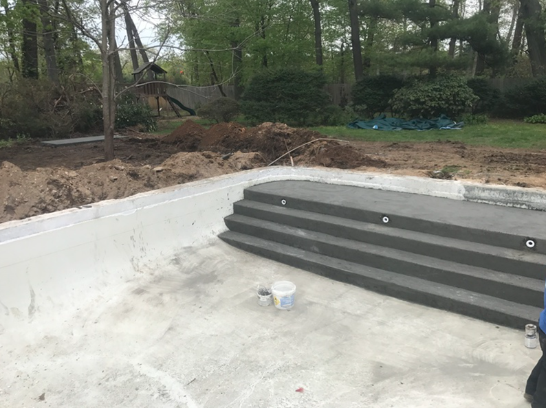 Concrete pool under construction, with steps and surrounding dirt.
