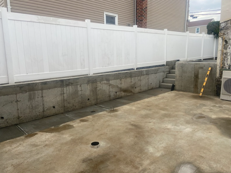 Concrete patio with white fence on raised foundation. Steps lead up to the fence.