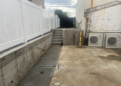 Concrete alleyway with steps, white fence, and air conditioning units.