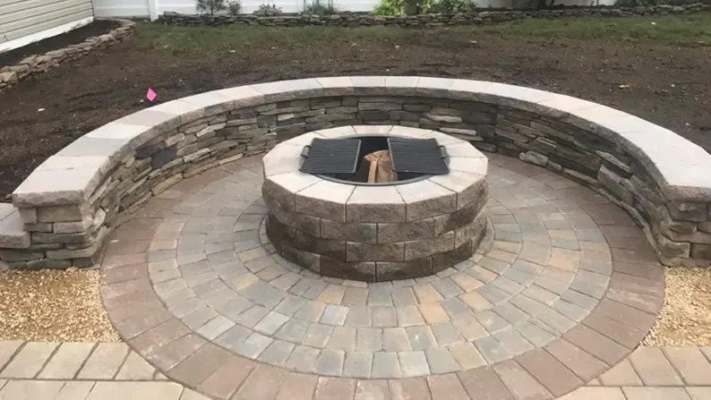 Stone fire pit with curved wall and circular brick patio in a yard.