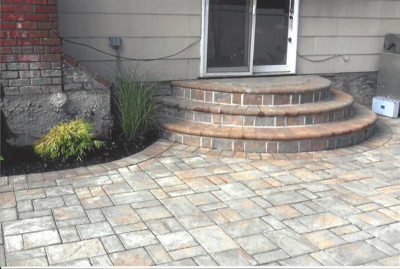 Patio with brick steps leading to sliding glass door. Landscaping with plants and pavers.