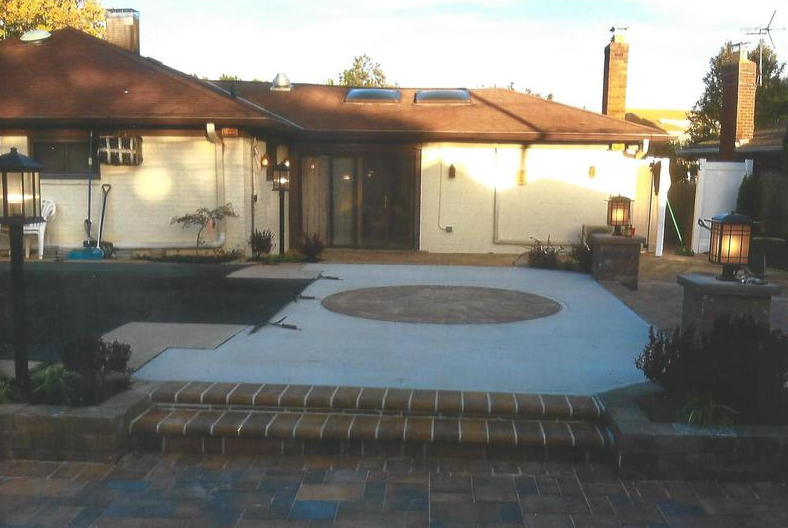 Backyard patio with pool, fire pit, and home with lanterns. Brown brick and tan siding.