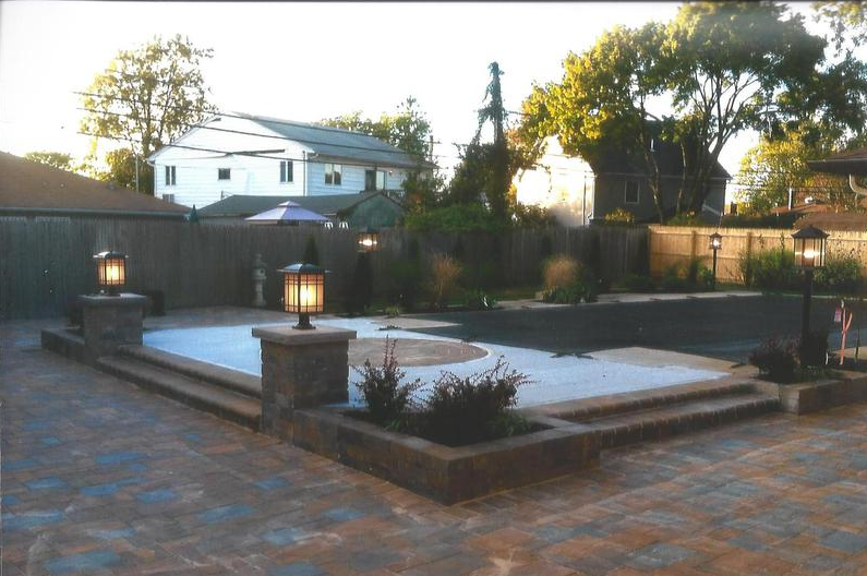 Backyard patio with pool, brickwork, and lit lanterns near homes.