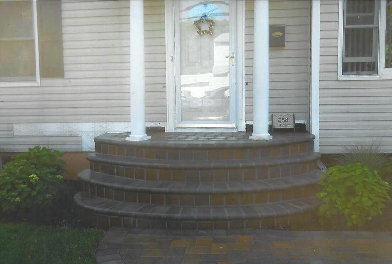Curved brick steps leading to a front door with white columns, flanked by green bushes.