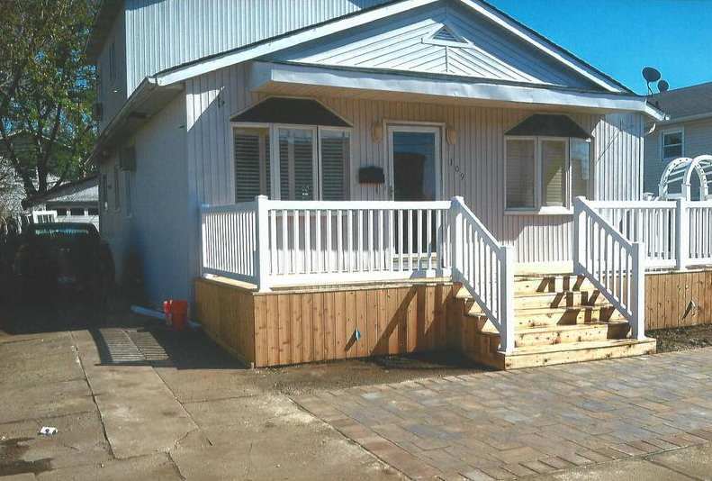 White house with a porch, wooden steps, and a paved driveway.