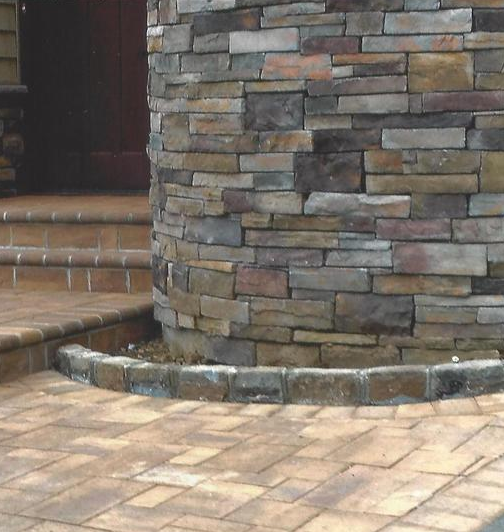 Stone pillar curves out of paved walkway, near steps and a dark door.
