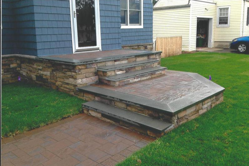 Stone steps and walkway leading to a blue house with green grass lawn.