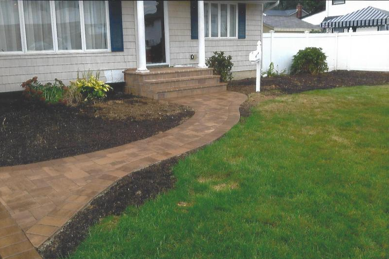 Brick walkway leading to house entrance with front steps and green lawn.