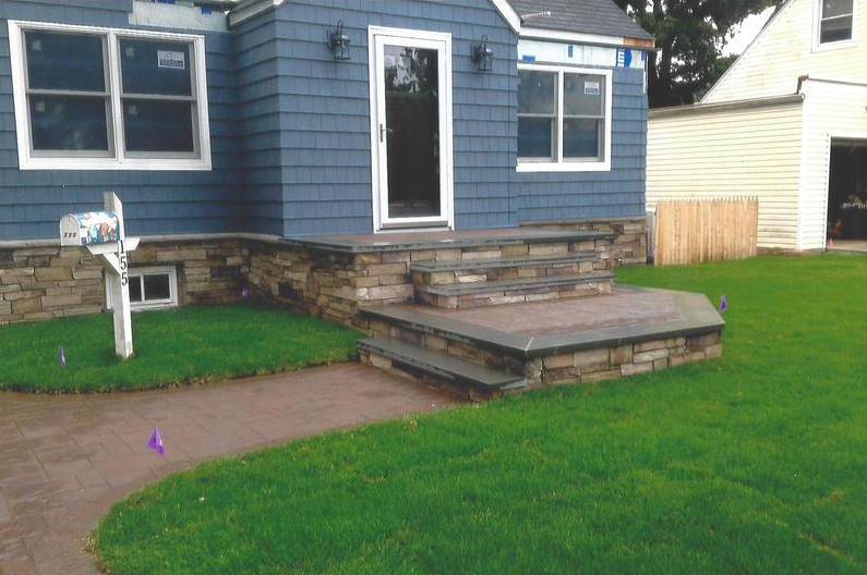 Blue house with stone steps and path leading to the front door, green lawn.