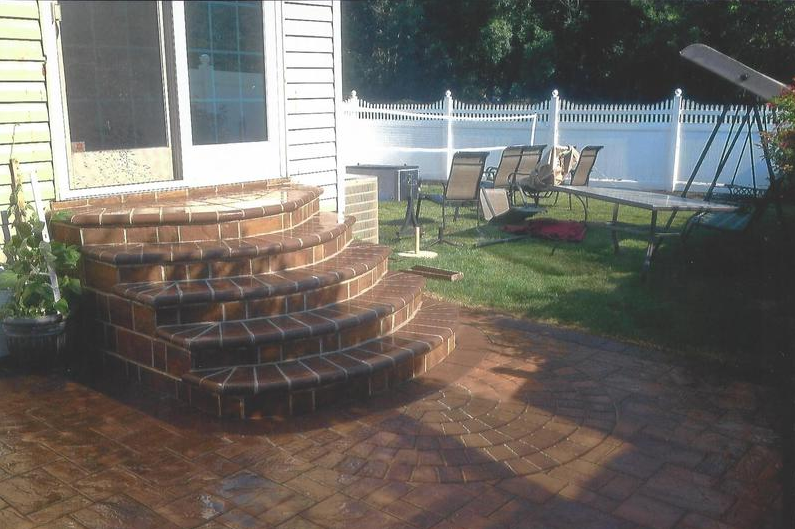 Brick steps leading to a doorway, brick patio. Chairs and white fence visible in background.