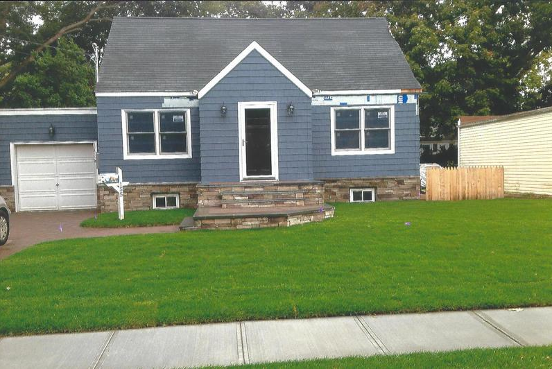 Blue house with white trim, garage, small stone porch, and green lawn.