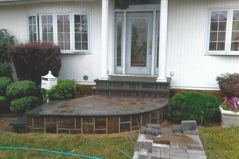 Brick steps lead to a house's front door, surrounded by bushes and a small garden.