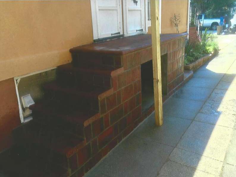 Brick steps lead to a doorway; a ramp is to the right. An attached building has an orange stucco wall.