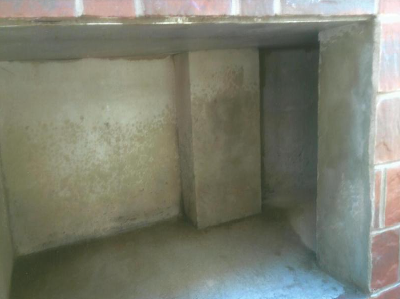 Interior of a brick fireplace under construction. Walls and floor are concrete; a central support stands.