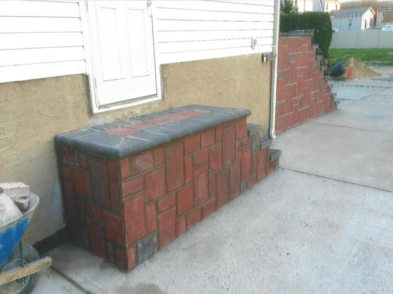 Brick steps leading to a door, next to a brick retaining wall and concrete ground.