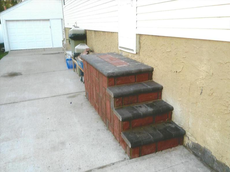 Brick steps leading to a house entrance. Concrete pathway and white garage are visible.
