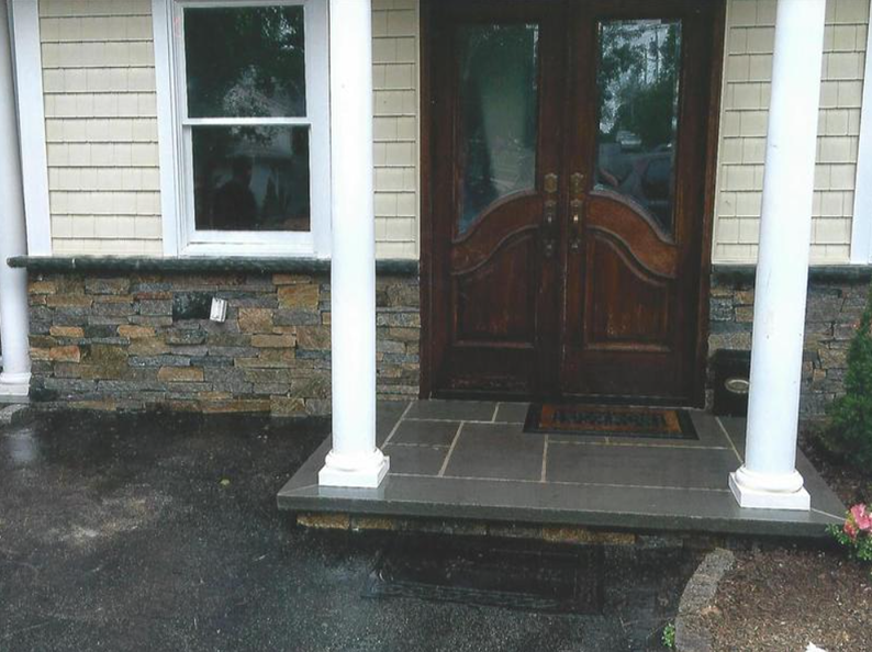 Front entrance with stone-clad facade and dark double doors; stone steps, white pillars, and a window.