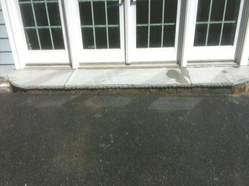 Stone threshold in front of white French doors, against asphalt.