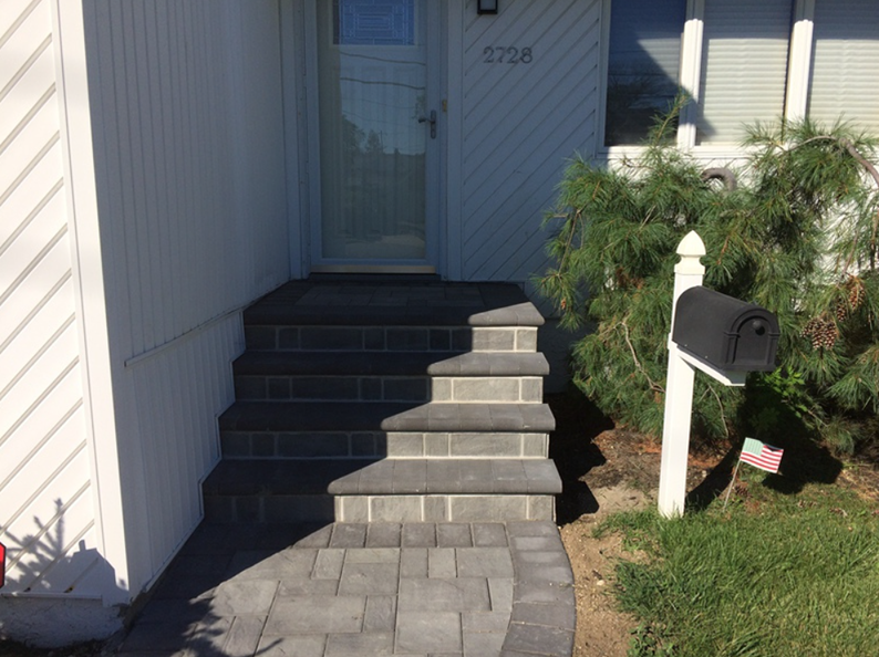Gray brick steps leading up to a house with a white door and a mailbox.