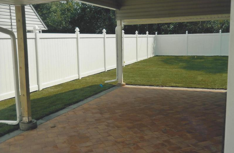Backyard with a white fence, green grass, and a concrete patio.