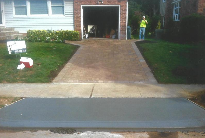 Driveway construction; new concrete leading to brick paved driveway and garage. Person standing at top right.