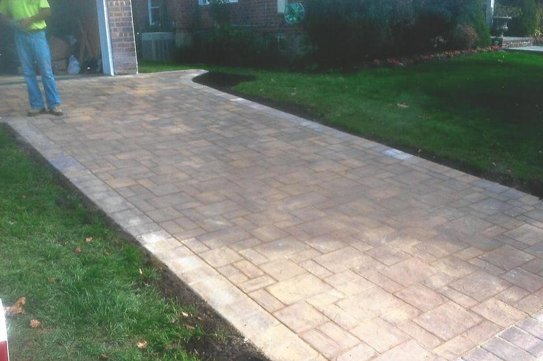 Brick driveway with green grass border, person standing near the garage.