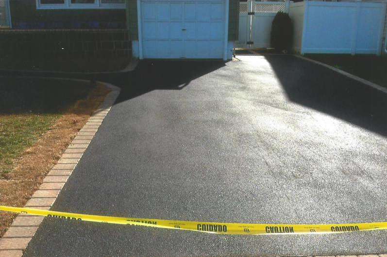 Newly sealed black asphalt driveway blocked with yellow caution tape.