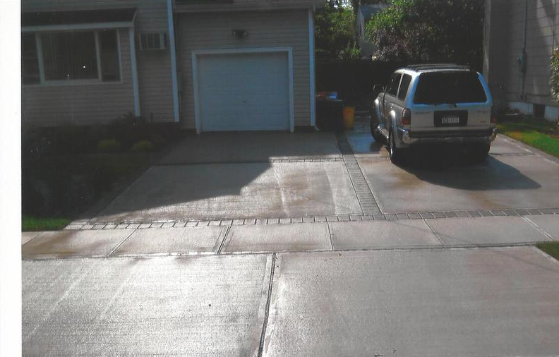 A silver SUV parked in a concrete driveway in front of a house with a garage.