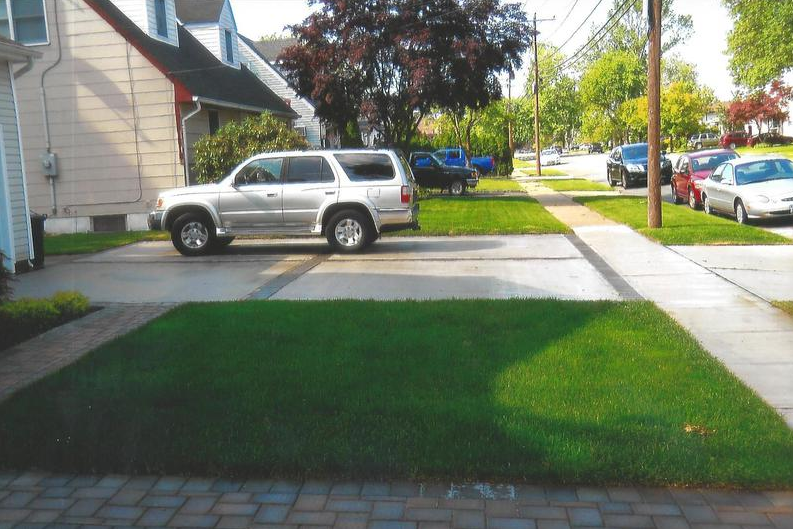 Silver SUV parked in a driveway next to a green lawn and sidewalk in a residential neighborhood.