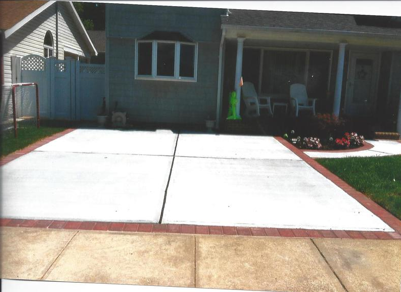 A concrete patio with brick border. A house in the background.