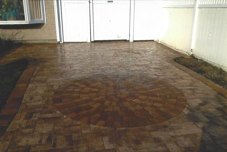 Brick patio with a circular design in front of garage doors.