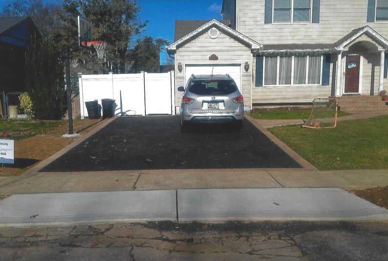 A silver SUV parked in a freshly paved driveway in front of a two-story house on a sunny day.