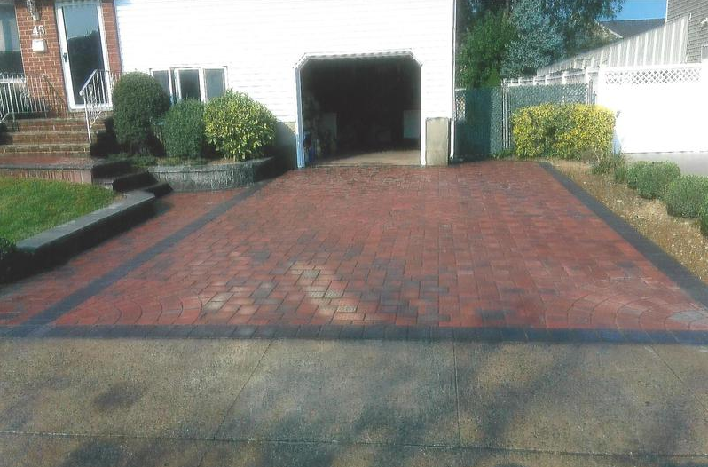 Brick driveway leading to a garage, bordered by dark paving stones and greenery.