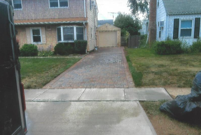 Driveway leading to a garage, flanked by lawns and houses on either side.