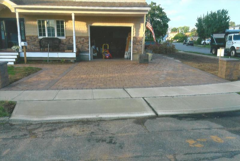 Tan house with garage, decorative driveway, sidewalk, street.
