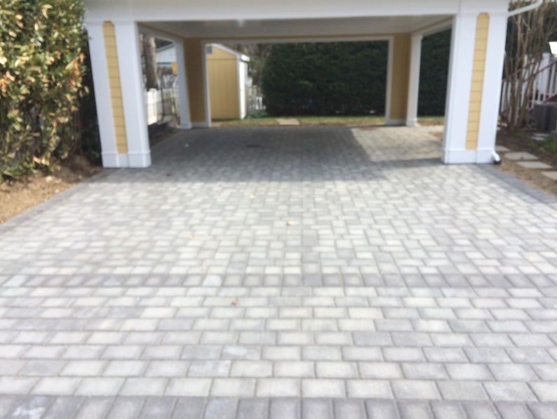 Brick driveway leading into a carport; columns and trim are painted white and yellow.